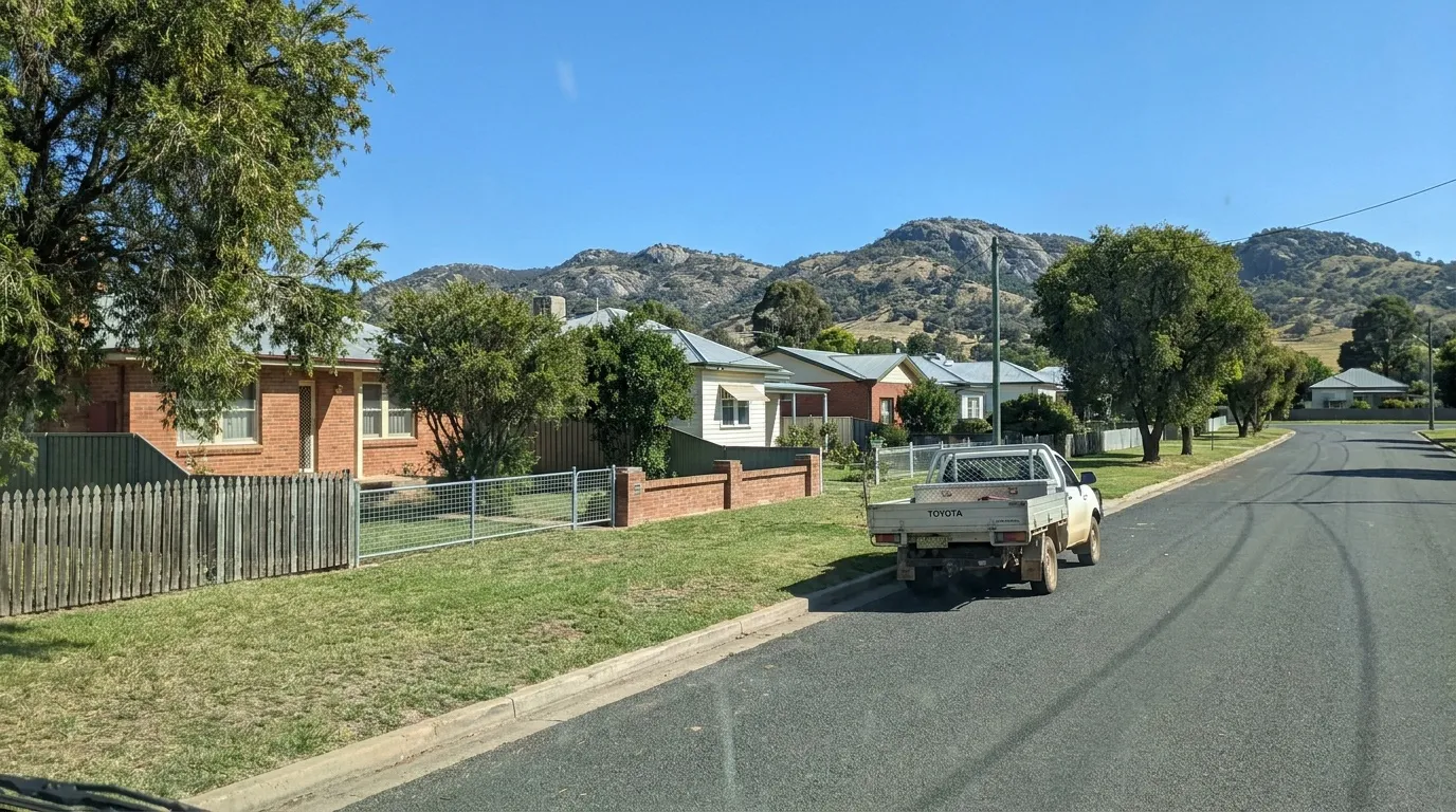Residential street of brick homes with front fences and granite hills behind